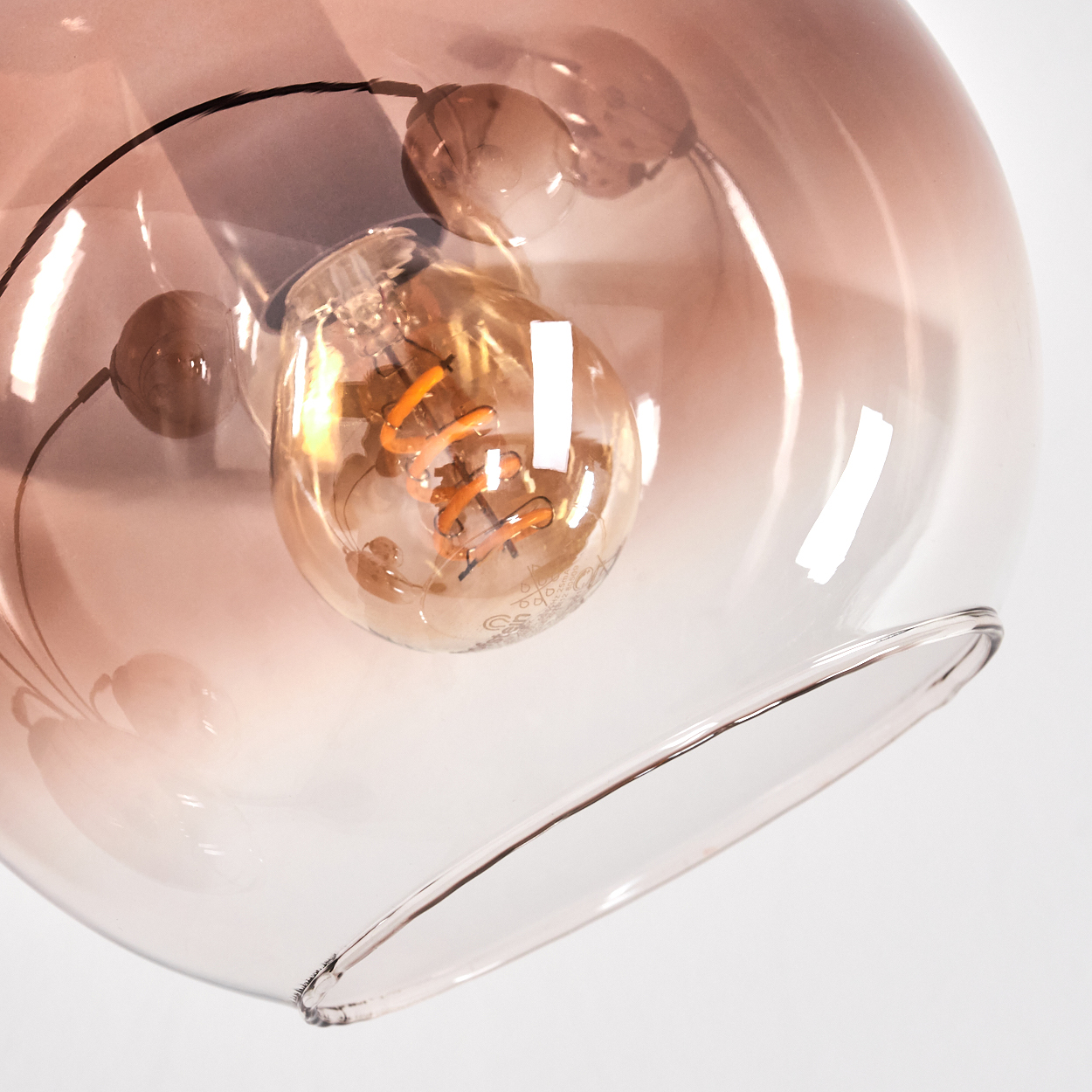 Nahaufnahme einer Glasleuchte. Die Glühbirne ist im transparenten Glasschirm sichtbar. Sie hat einen warmen, orangefarbenen Schein.