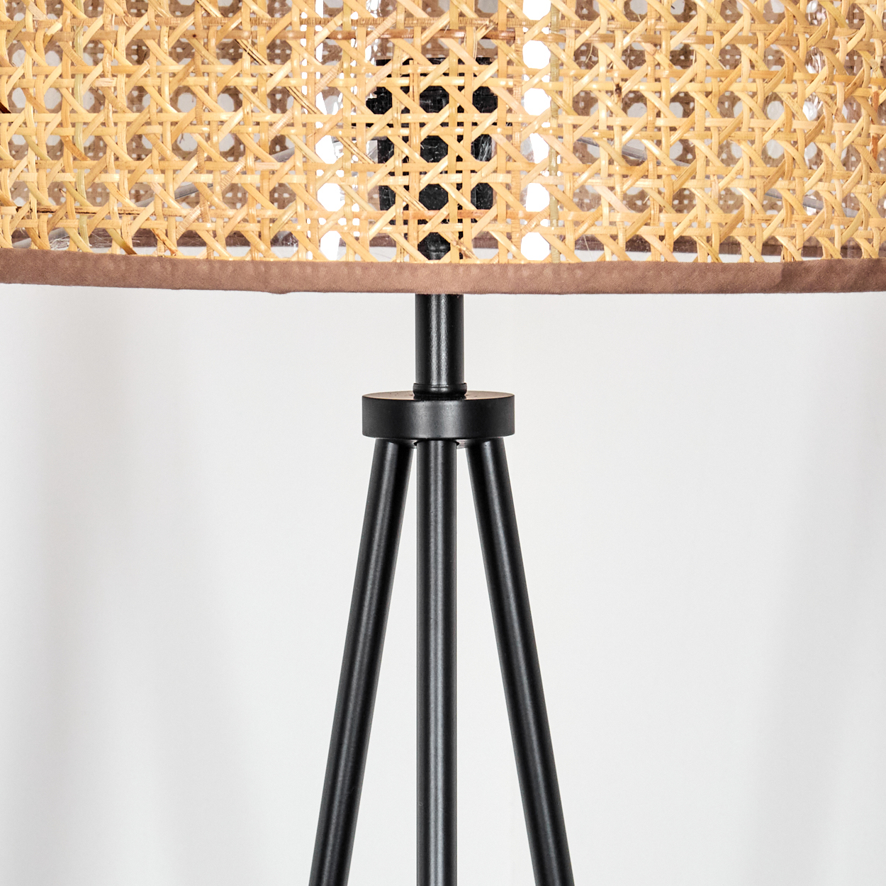 Nahaufnahme einer Lampe. Die Lampe hat einen gewebten Rattanschatten mit braunem Rand, der von einem schwarzen Stativfuß getragen wird.