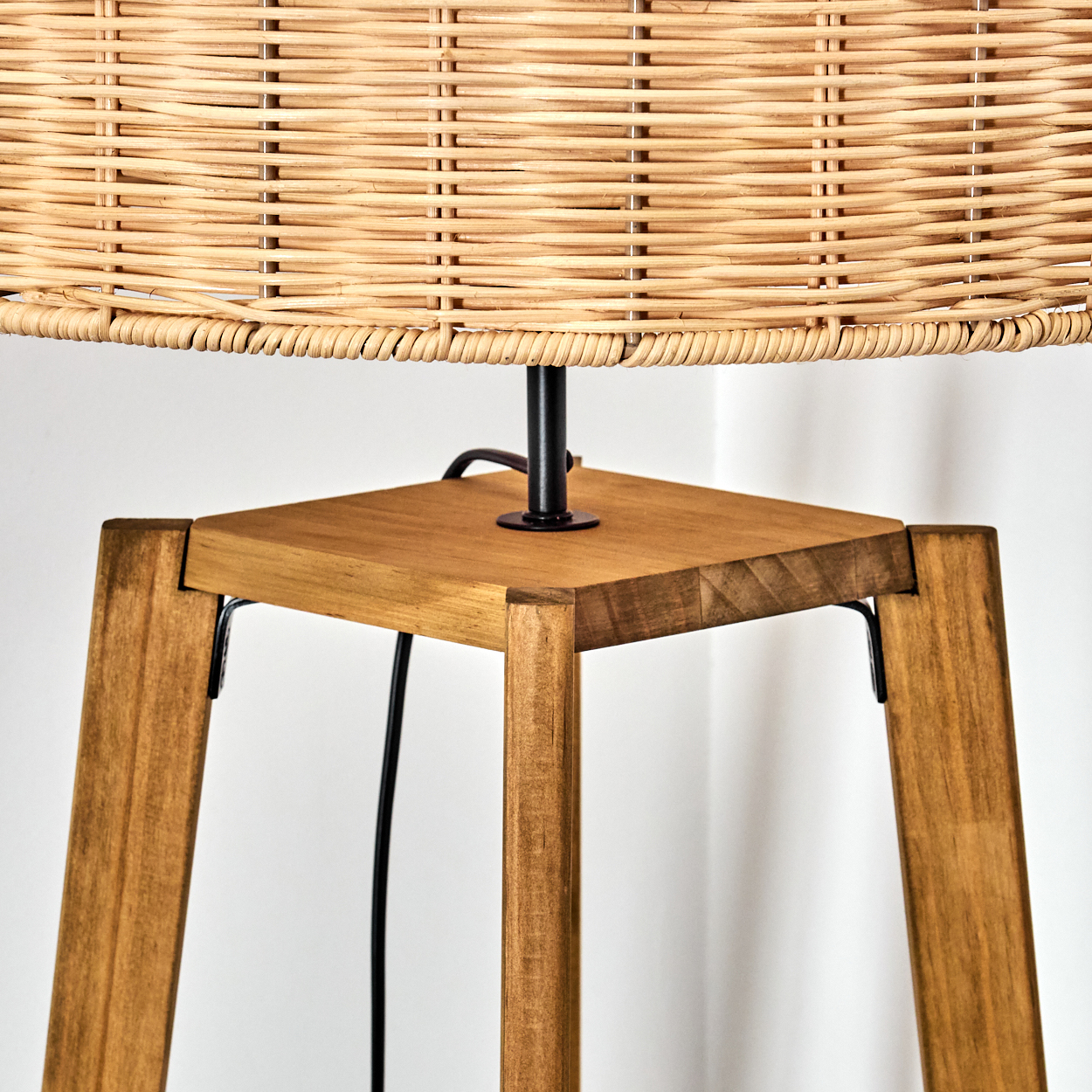 Nahaufnahme einer Lampe. Sie hat einen gewebten Lampenschirm und einen Holzsockel mit quadratischer Oberseite und abgewinkelten Beinen.