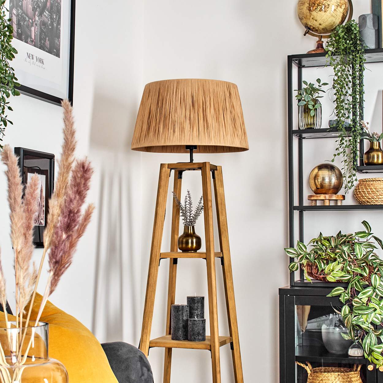 Ein Raum mit einer Holzlampe, einem Regal, Pflanzen und Kerzen. Ein New York-Bild hängt an der Wand, und ein gelbes Sofa ist in der Ecke.