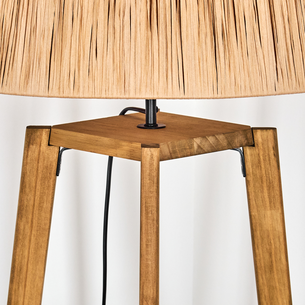 Eine Holzlampe mit gewebtem Lampenschirm. Die Lampe hat vier Holzbeine und eine quadratische Basis. Ein schwarzes Kabel erstreckt sich nach unten.