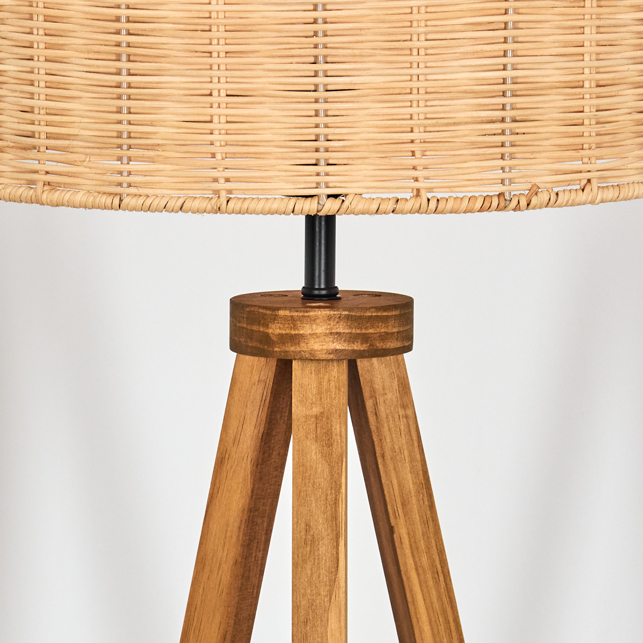 Nahaufnahme einer Holz-Stativlampe. Die Lampe hat einen gewebten Lampenschirm, einen schwarzen Metallträger und einen hellen Holzsockel.