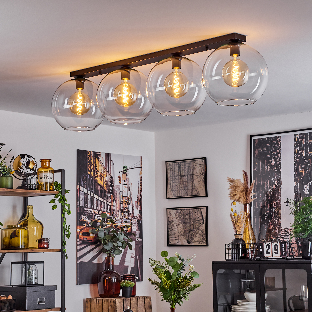 Ein modernes Zimmer mit einer Deckenleuchte mit vier Glaskugeln. Kunstwerke und Dekoration an den Wänden und Regalen.