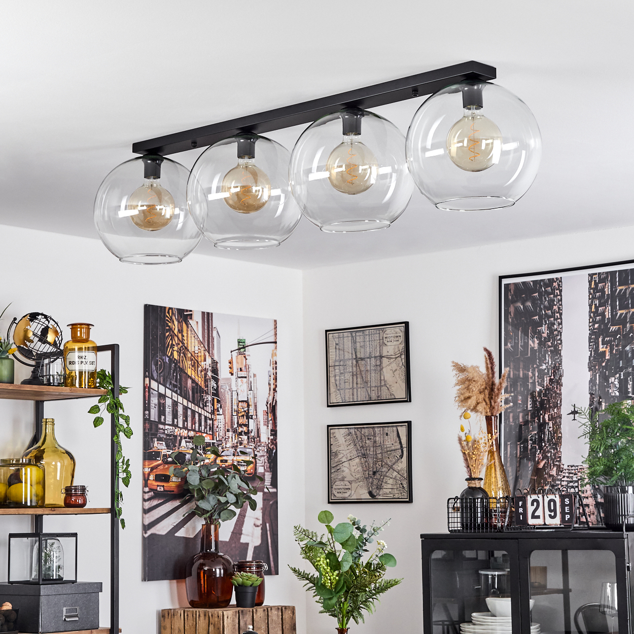 Ein modernes Wohnzimmer mit einer schwarzen Deckenlampe mit vier Glühbirnen. Kunstwerke und Dekorationsartikel sind vorhanden.