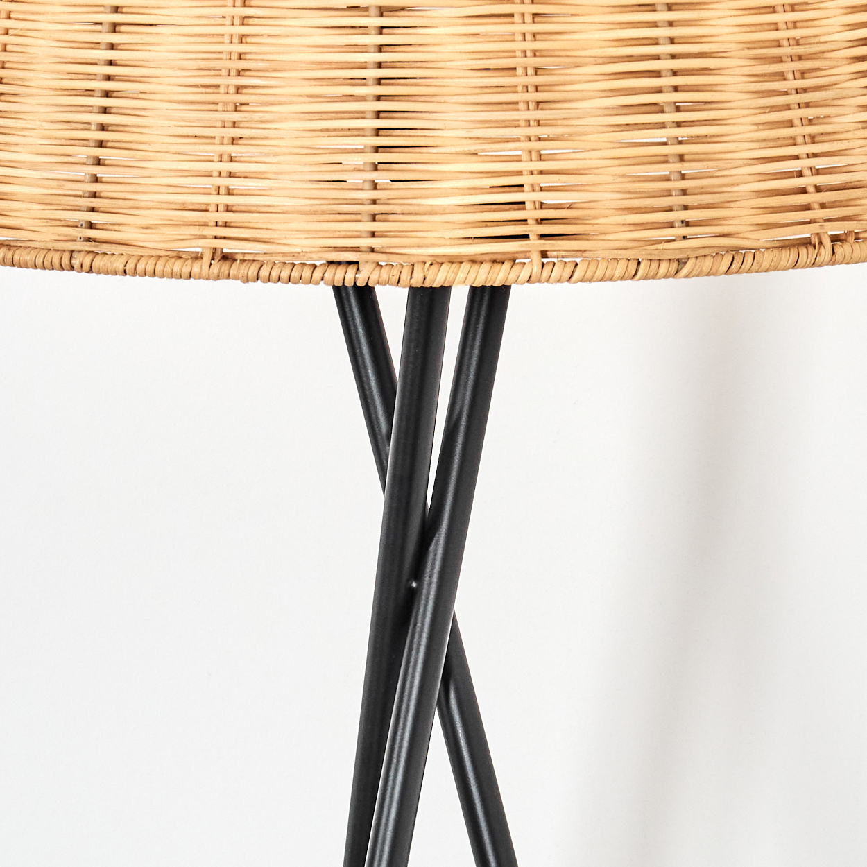 Nahaufnahme einer Lampe. Gewebter hellbrauner Lampenschirm auf schwarzen Metallbeinen. Weißer Hintergrund.