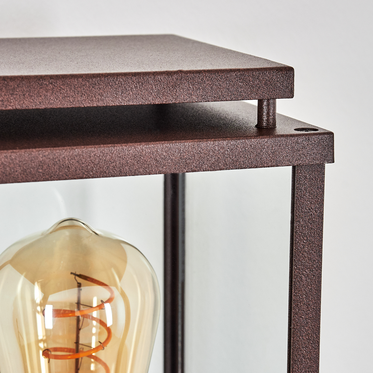 Nahaufnahme einer Lampe. Sie hat einen bronzefarbenen Rahmen, Glasseiten und eine große, warm getönte Glühbirne.