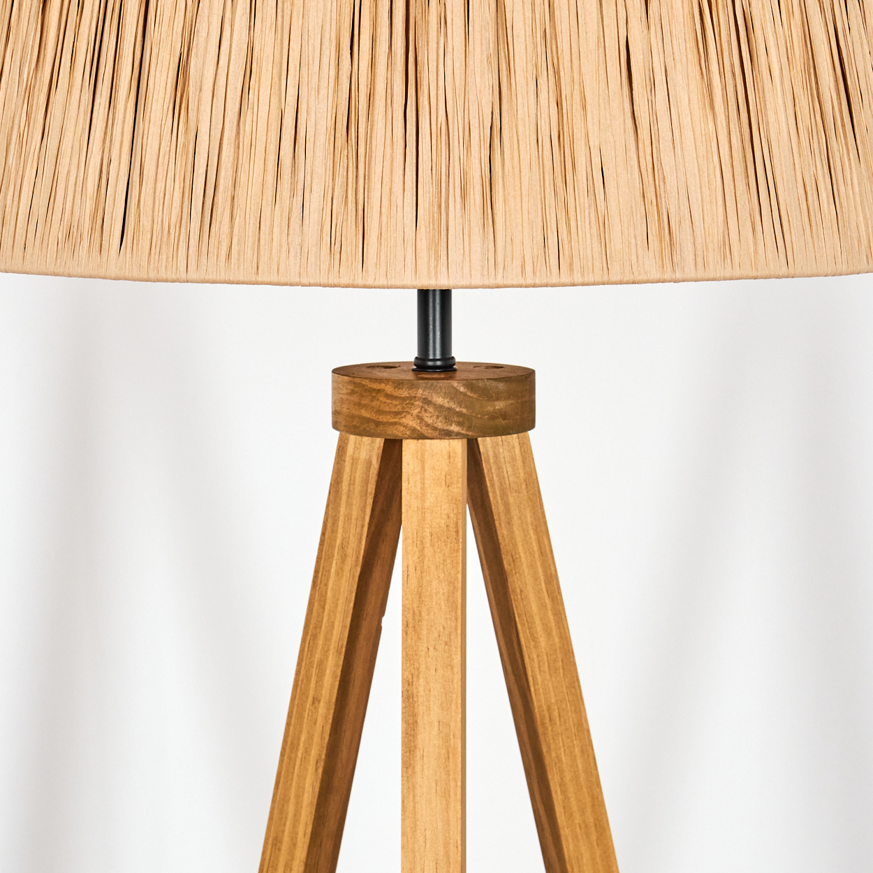 Nahaufnahme einer Stehlampe. Sie hat einen beigefarbenen Lampenschirm, Holzbeine und eine dunkle Metallstange. Der Hintergrund ist weiß.
