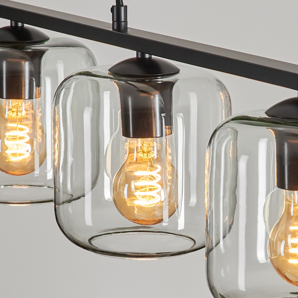 Nahaufnahme einer modernen Leuchte. Drei klare Glasschirme mit Edison-Glühbirnen hängen an einem schwarzen Metallrahmen.
