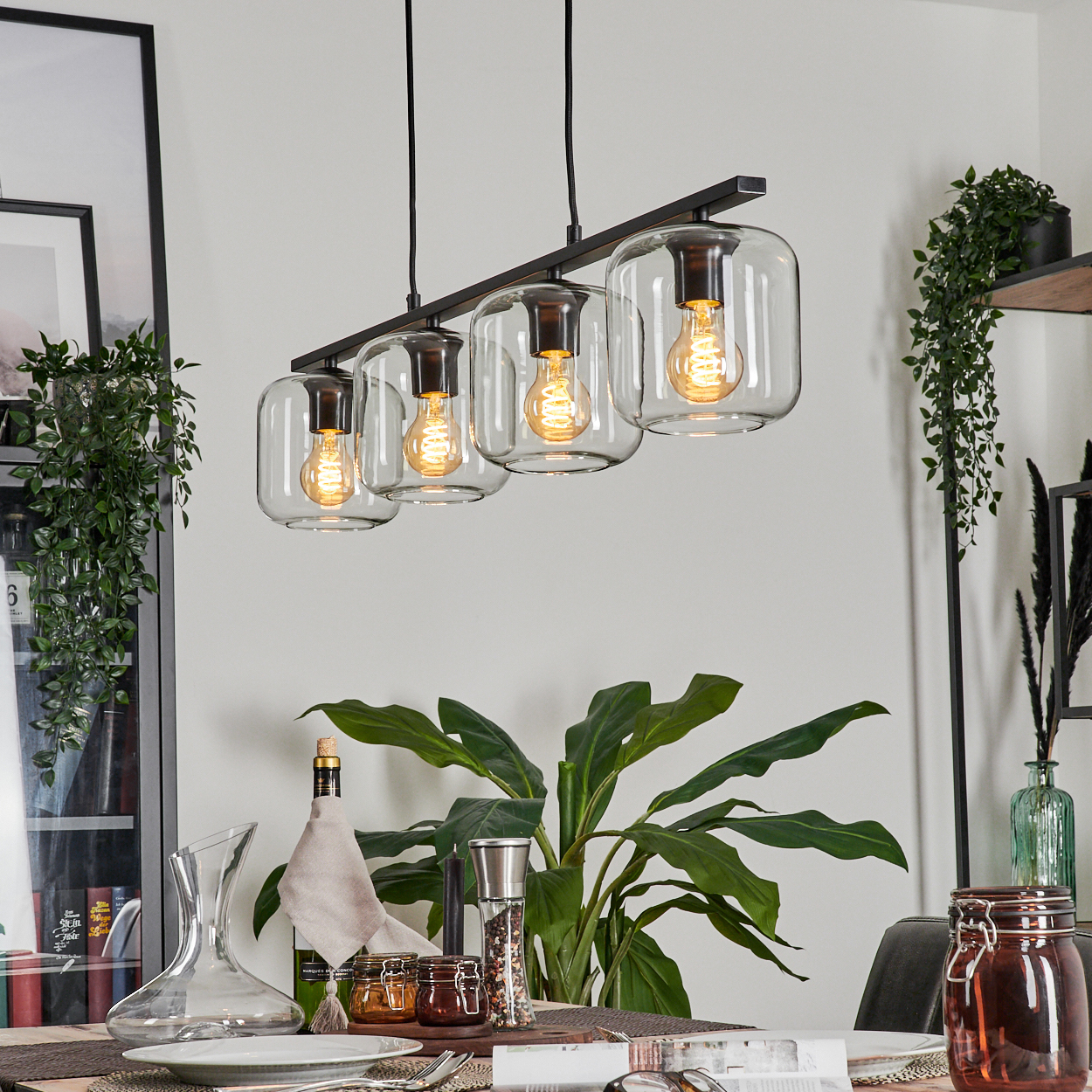 Esszimmer mit Hängeleuchte. Die Leuchte hat vier Glasschirme mit beleuchteten Glühbirnen. Ein Esstisch ist gedeckt.