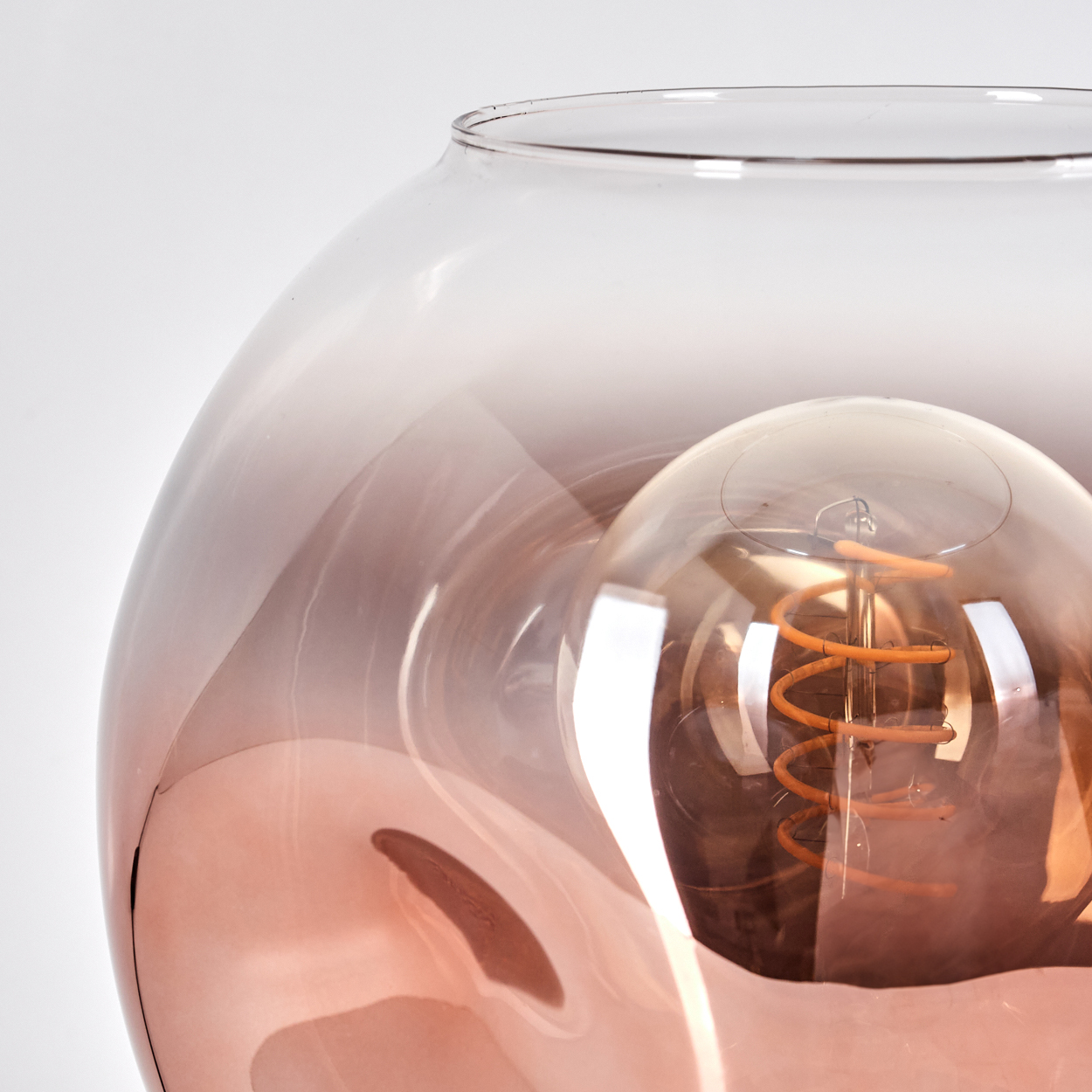 Nahaufnahme einer Glaslampe mit Glühbirne. Das Glas ist klar mit rosa Farbton. Die Glühbirne hat einen Spiralglühfaden.