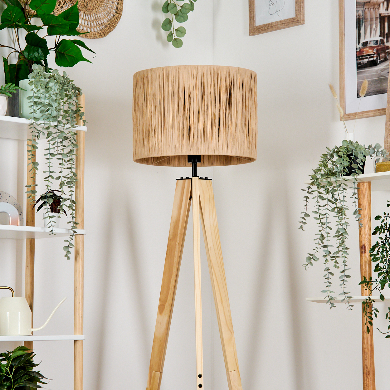 Ein beiger Lampenschirm steht auf einem Holzstativ. Links und rechts sind Regale mit Pflanzen. Im Hintergrund hängt ein Bild.