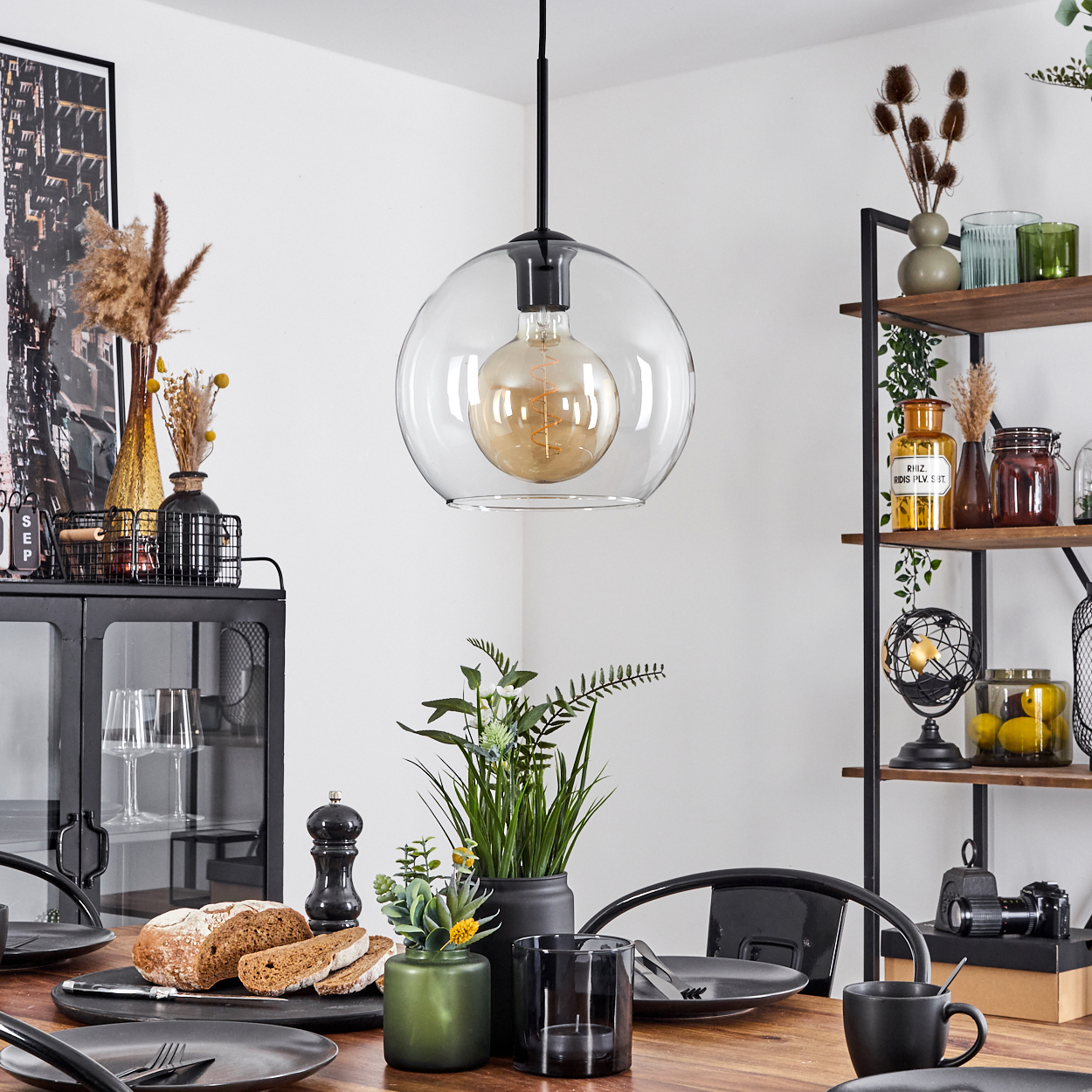 Esszimmer mit Holztisch, Brot, Tellern und einer Hängeleuchte. Regale mit Dekorationen sind im Hintergrund.