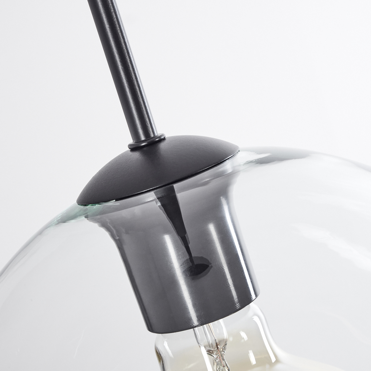 Nahaufnahme einer schwarzen Lampenhalterung mit Glaskolben. Das Glas ist klar, der Hintergrund ist weiß.