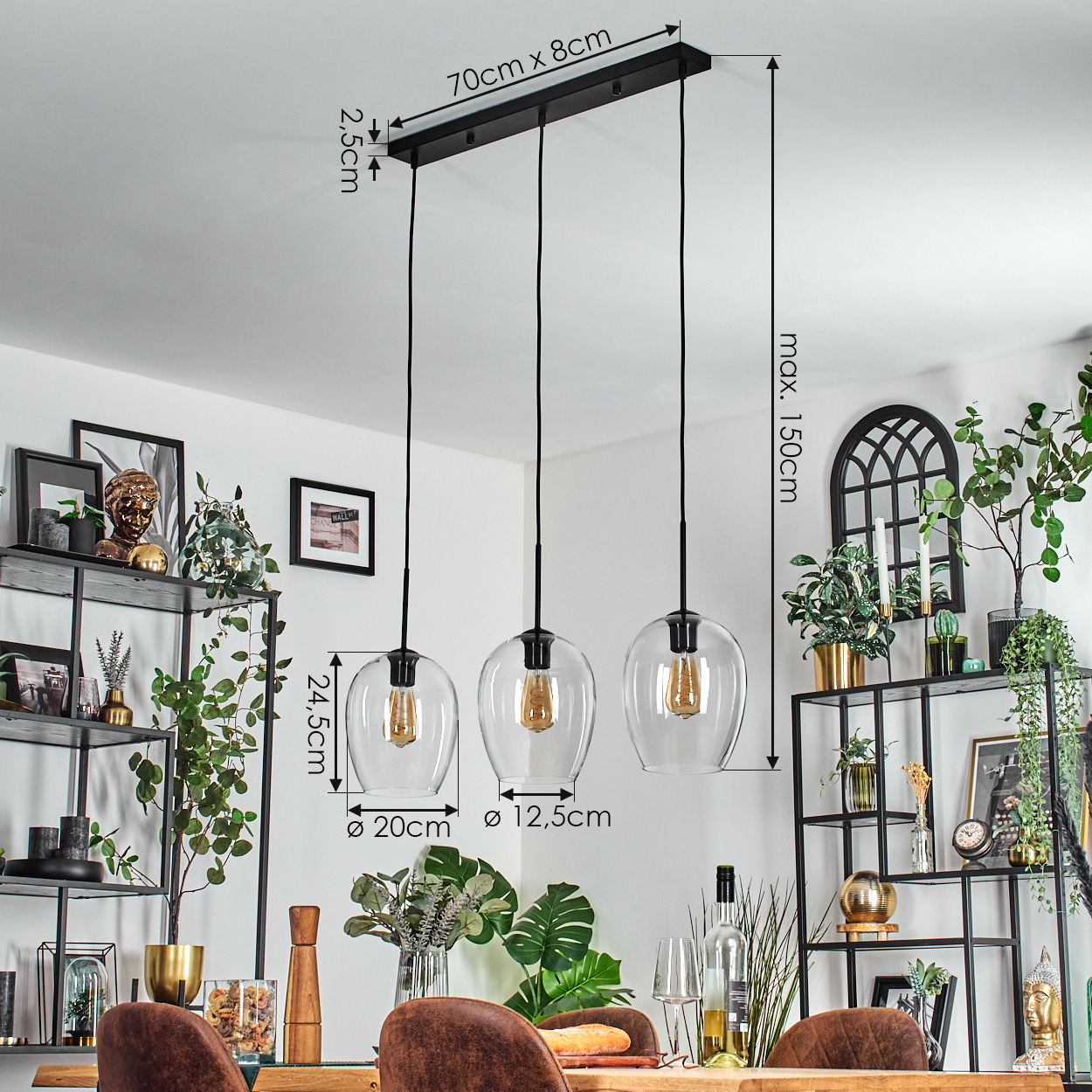 Ein Esszimmer mit einer schwarzen Leuchte mit drei Glas-Pendelleuchten. Es gibt Pflanzen und einen Tisch mit Weingläsern.
