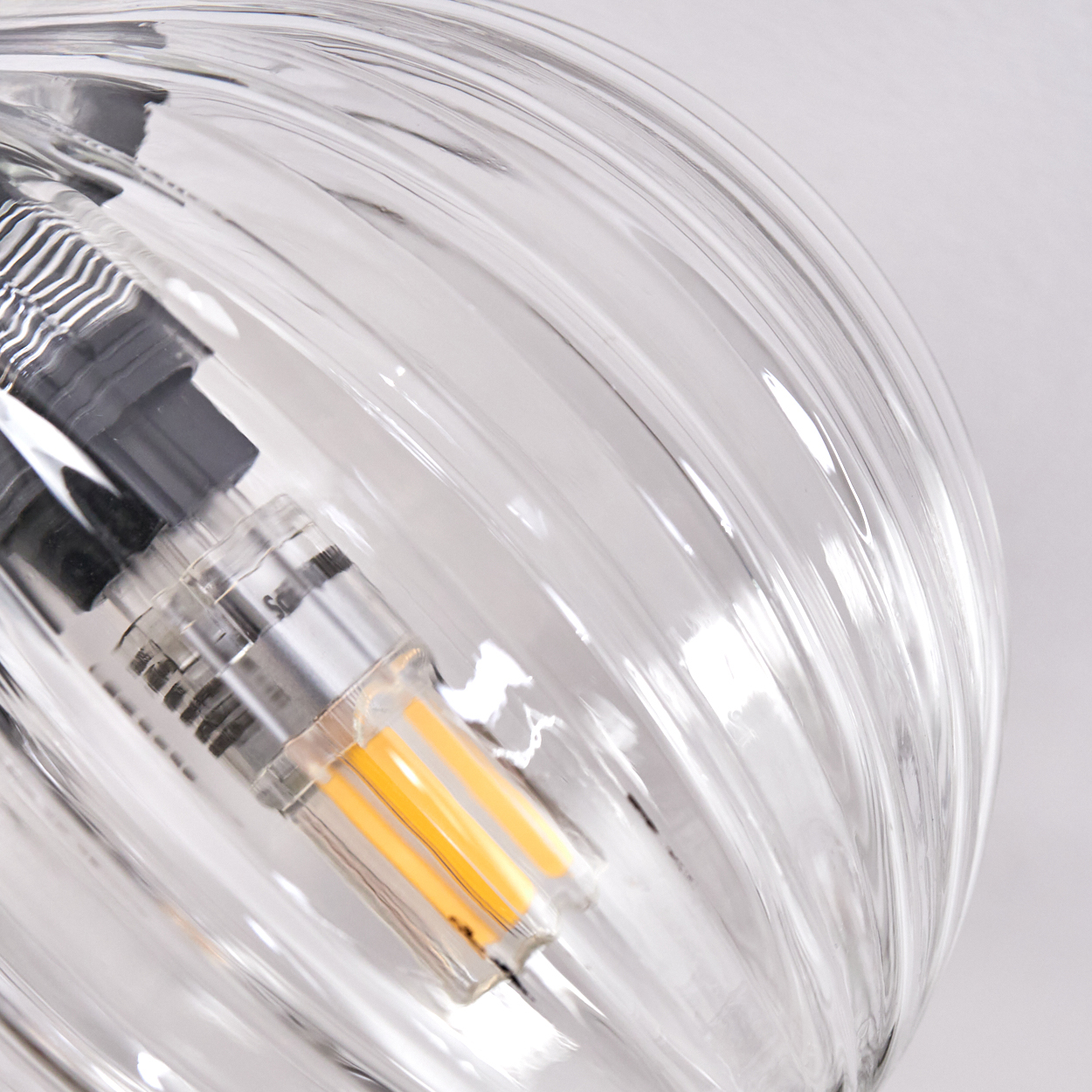 Nahaufnahme einer Glasleuchte. Das klare, geriffelte Glas umgibt ein orangefarbenes LED-Licht. Der Hintergrund ist weiß.