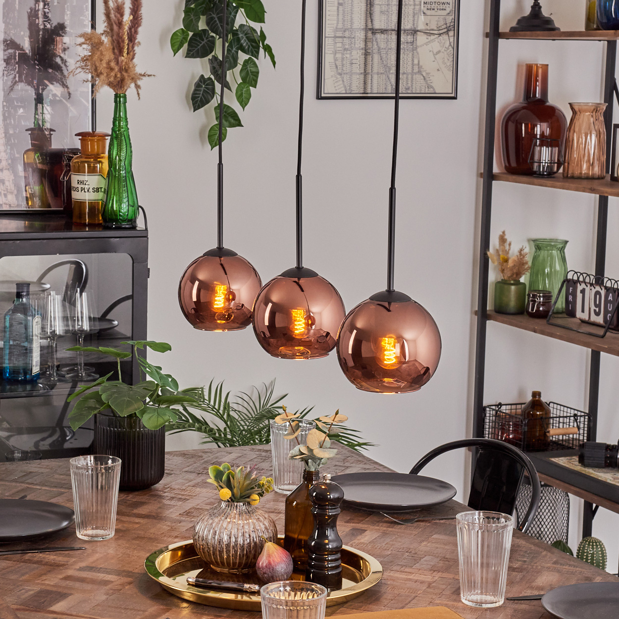 Esszimmer mit kupferfarbenen Pendelleuchten über einem Holztisch mit Tellern, Gläsern und Dekoration.