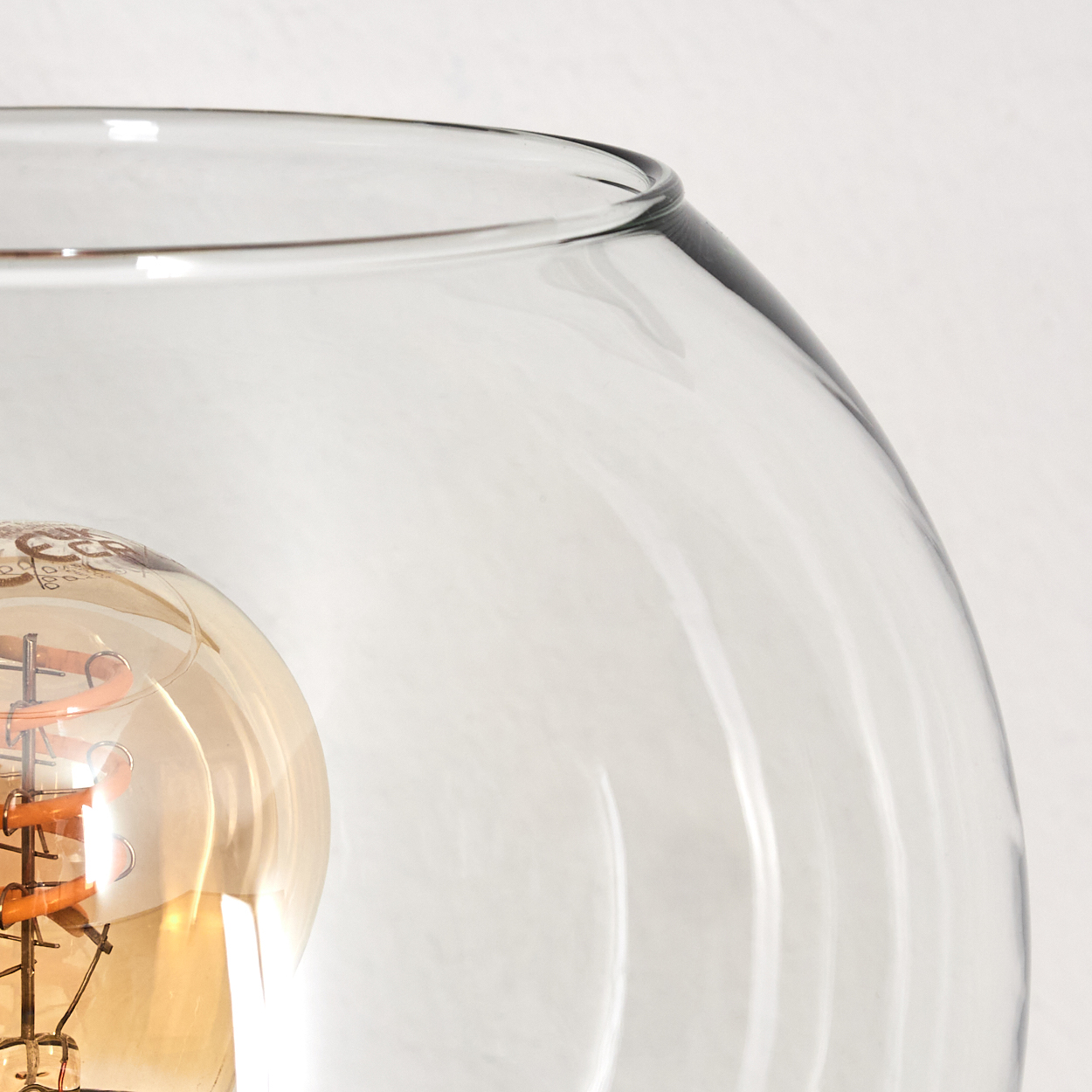 Nahaufnahme einer Glaslampe mit sichtbarer Glühbirne. Das Glas ist klar, und die Glühbirne leuchtet gelb, vor weißem Hintergrund.