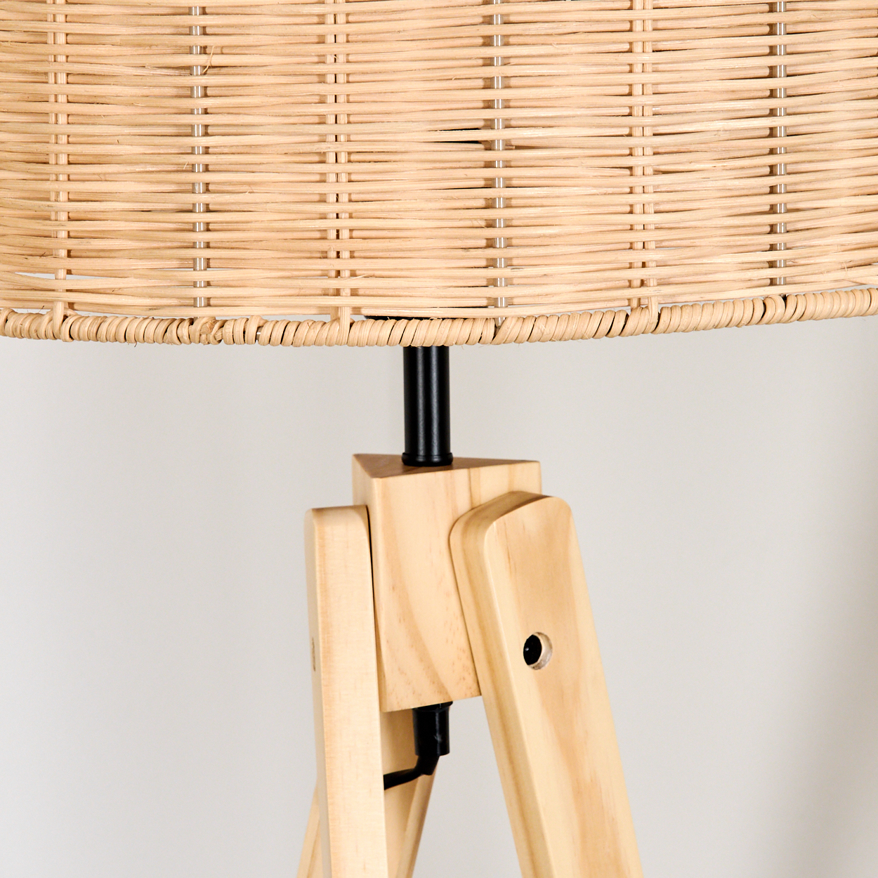 Nahaufnahme einer Lampe. Sie hat einen gewebten Lampenschirm auf einem Holzstativ. Der Hintergrund ist eine weiße Wand.