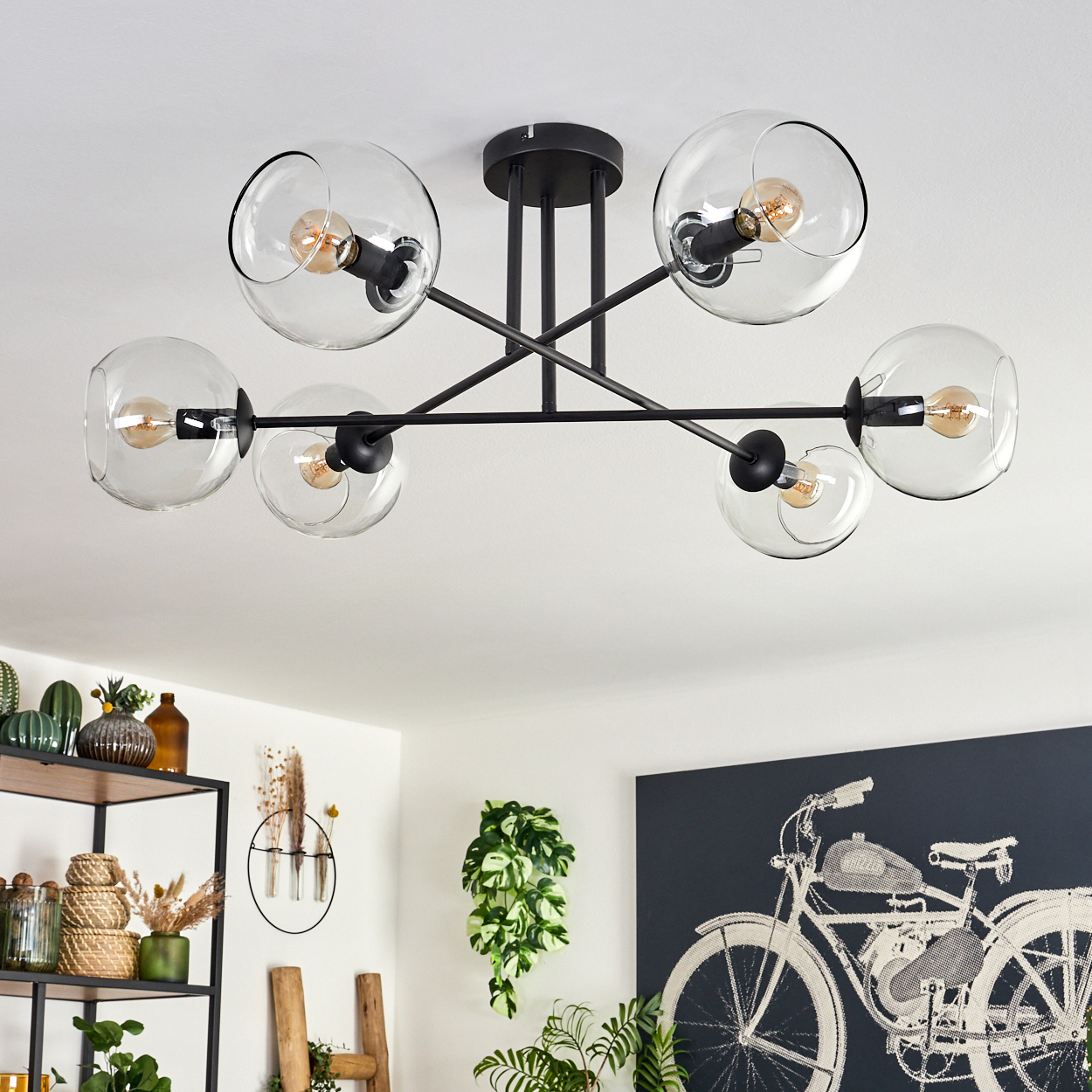 Eine moderne Deckenleuchte mit sechs Glaskugelschirmen. Der Raum hat ein Regal mit Pflanzen, ein Fahrradkunstwerk und eine grüne Pflanze.
