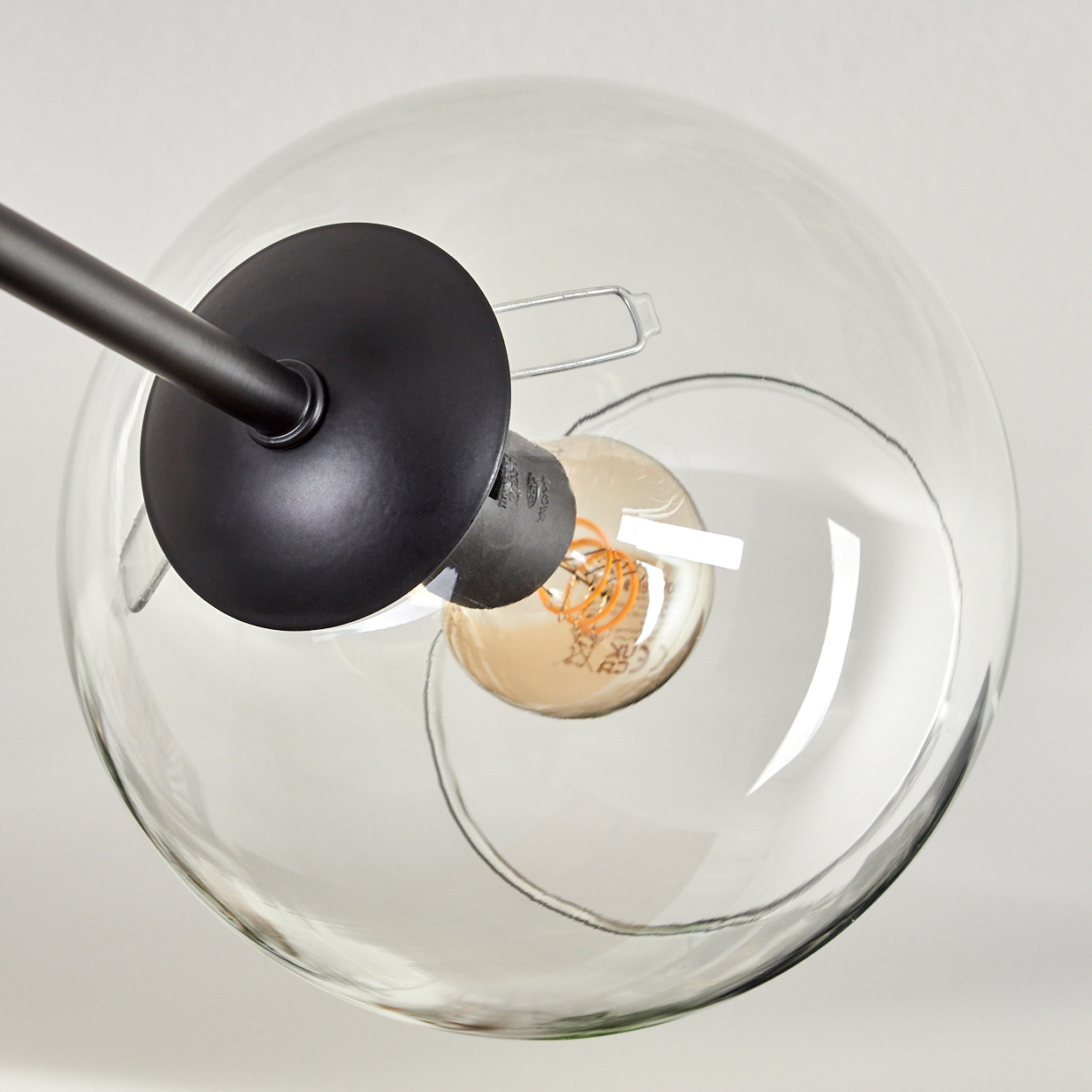 Nahaufnahme einer modernen Leuchte. Sie hat einen schwarzen Arm und einen runden, klaren Glasschirm. Im Inneren ist eine Glühbirne zu sehen.