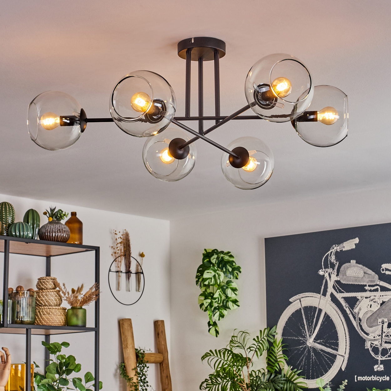 Eine moderne Deckenleuchte mit sechs kugelförmigen Lichtern. Der Raum hat Pflanzen, Dekorationen und ein Motorrad-Kunstwerk an der Wand.