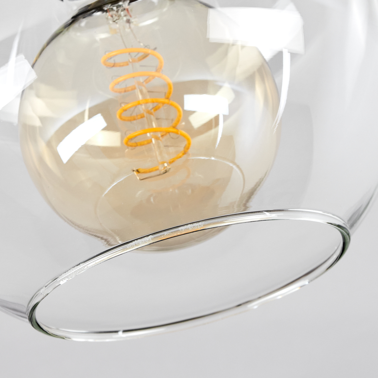 Nahaufnahme einer Leuchte. Ein klarer Glasschirm umgibt eine Glühbirne mit Spiralfaden. Der Hintergrund ist weiß.