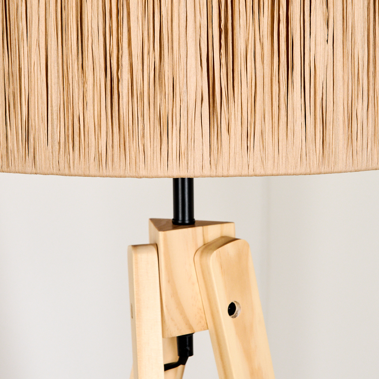 Ein beigefarbener Lampenschirm sitzt auf einer Holzstativlampe. Der Hintergrund ist eine schlichte weiße Wand.