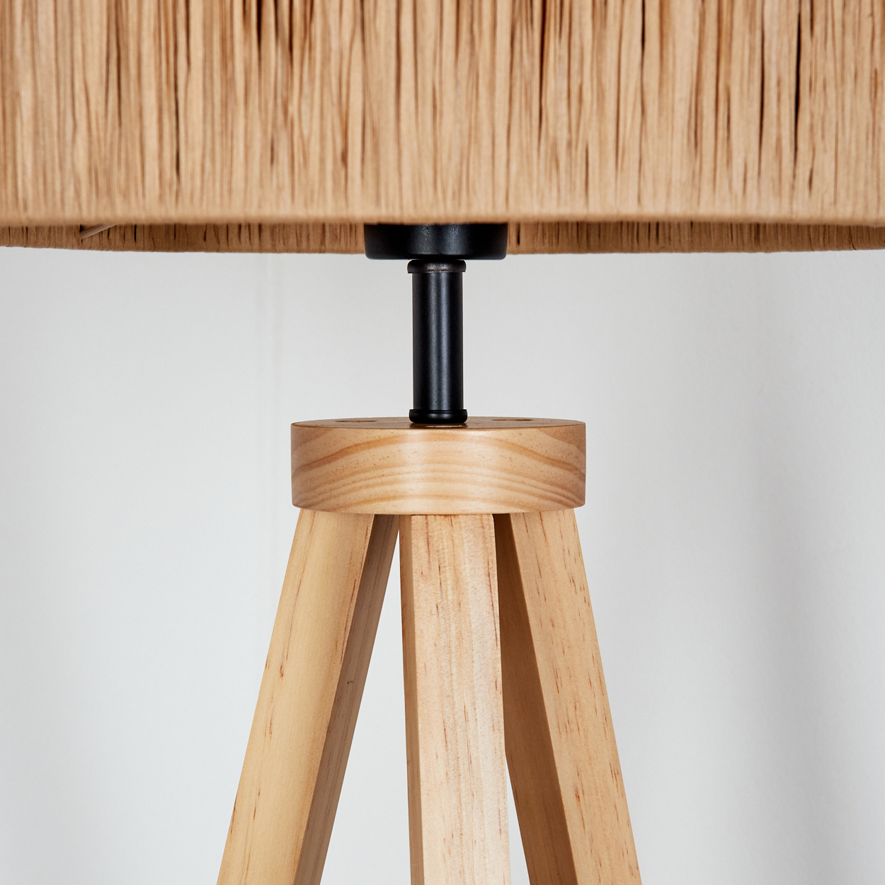 Nahaufnahme einer Lampe. Sie hat einen hellbraunen Schirm und Holzbeine. Der Schirm ist aus gewebtem Material und die Beine aus hellem Holz.