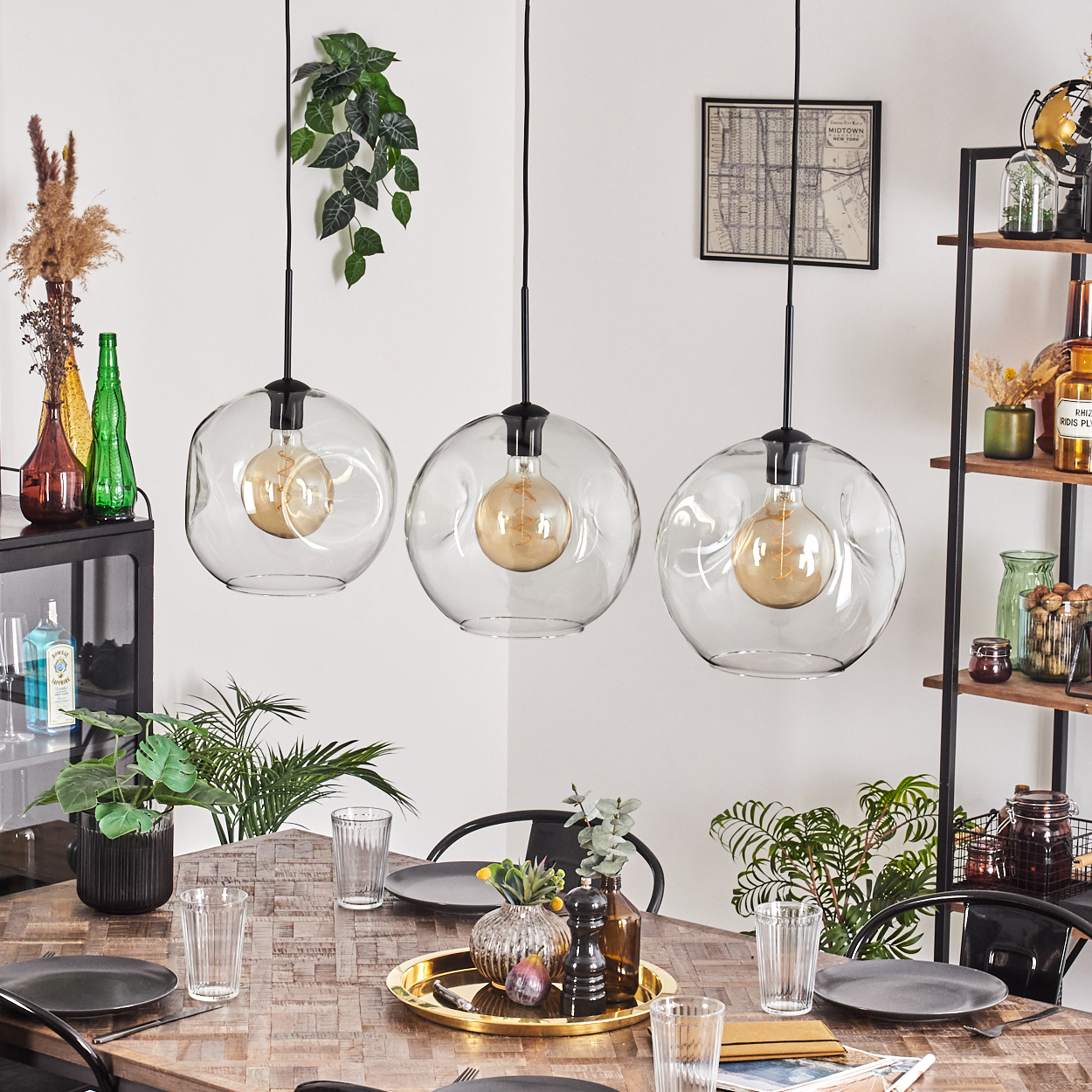Esszimmer mit drei Glaskugel-Pendelleuchten. Tisch mit Tellern, Gläsern und Dekoration. Regale mit verschiedenen Gegenständen.