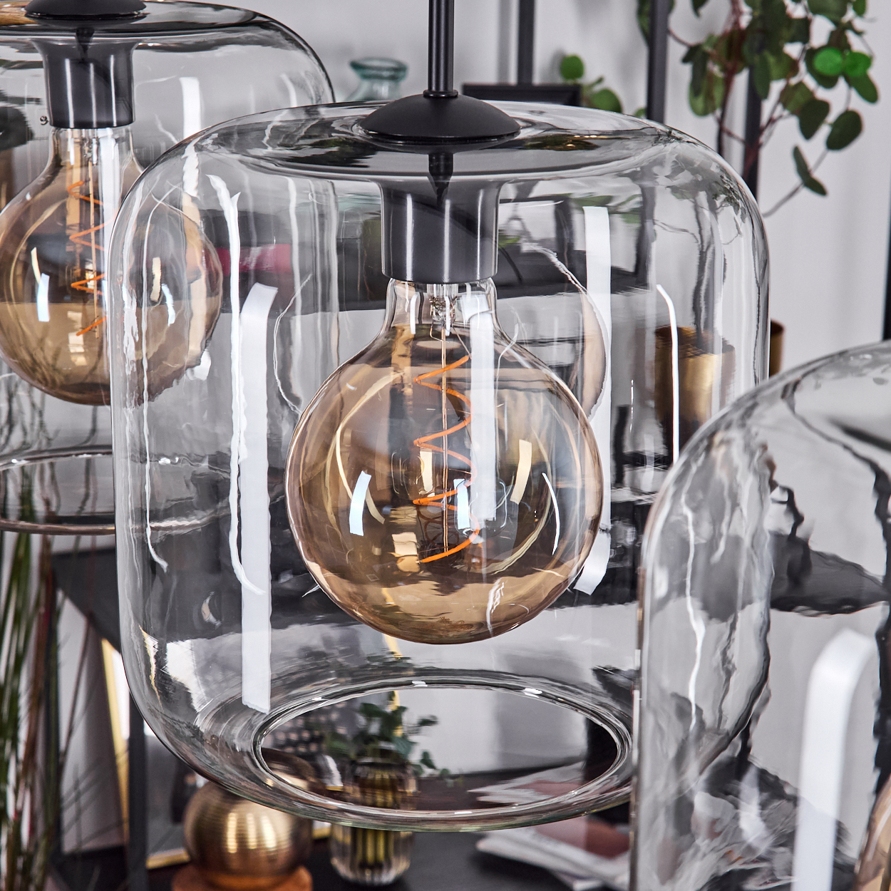 Nahaufnahme von drei Glas-Hängeleuchten mit warm getönten Glühbirnen. Die Glühbirnen sind in durchsichtigen Glasschirmen eingeschlossen.