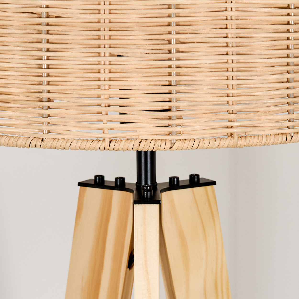 Nahaufnahme einer Lampe. Der Lampenschirm ist aus geflochtenem Korbgeflecht, über Holzbeinen. Die Beine sind helles Holz und der Rahmen ist aus schwarzem Metall.