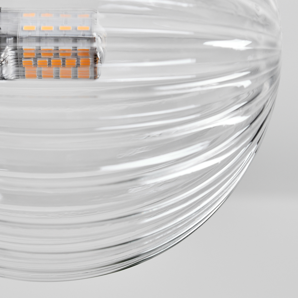 Nahaufnahme eines klaren, geriffelten Glasobjekts mit einem LED-Panel. Das Glas reflektiert Licht und erzeugt weiche Highlights. Der Hintergrund ist hellgrau.