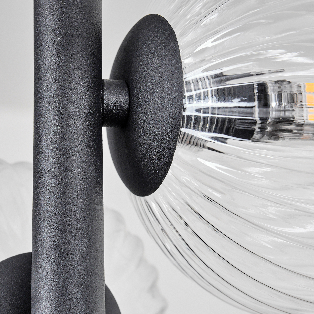 Nahaufnahme einer modernen Lampe. Ein schwarzer Metallrahmen trägt einen Glaskolben mit geripptem Muster. Weiche Beleuchtung sichtbar.