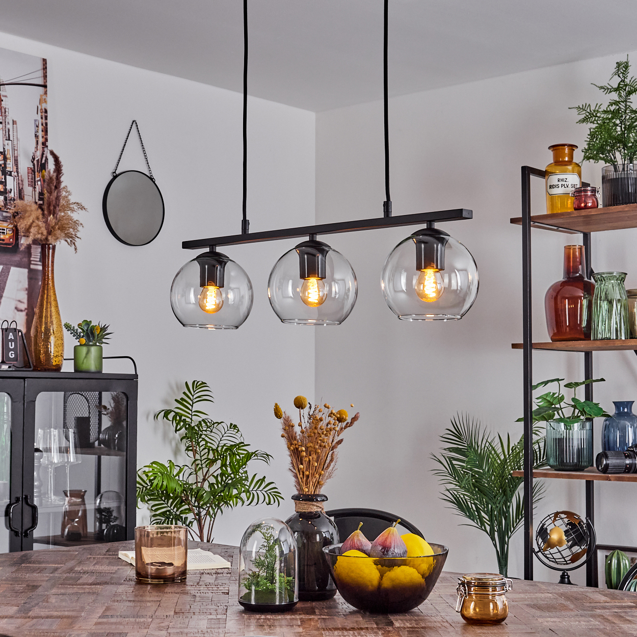 Ein Esszimmer mit Holztisch, dreifacher Leuchte und Dekoration wie Pflanzen und einem Globus.