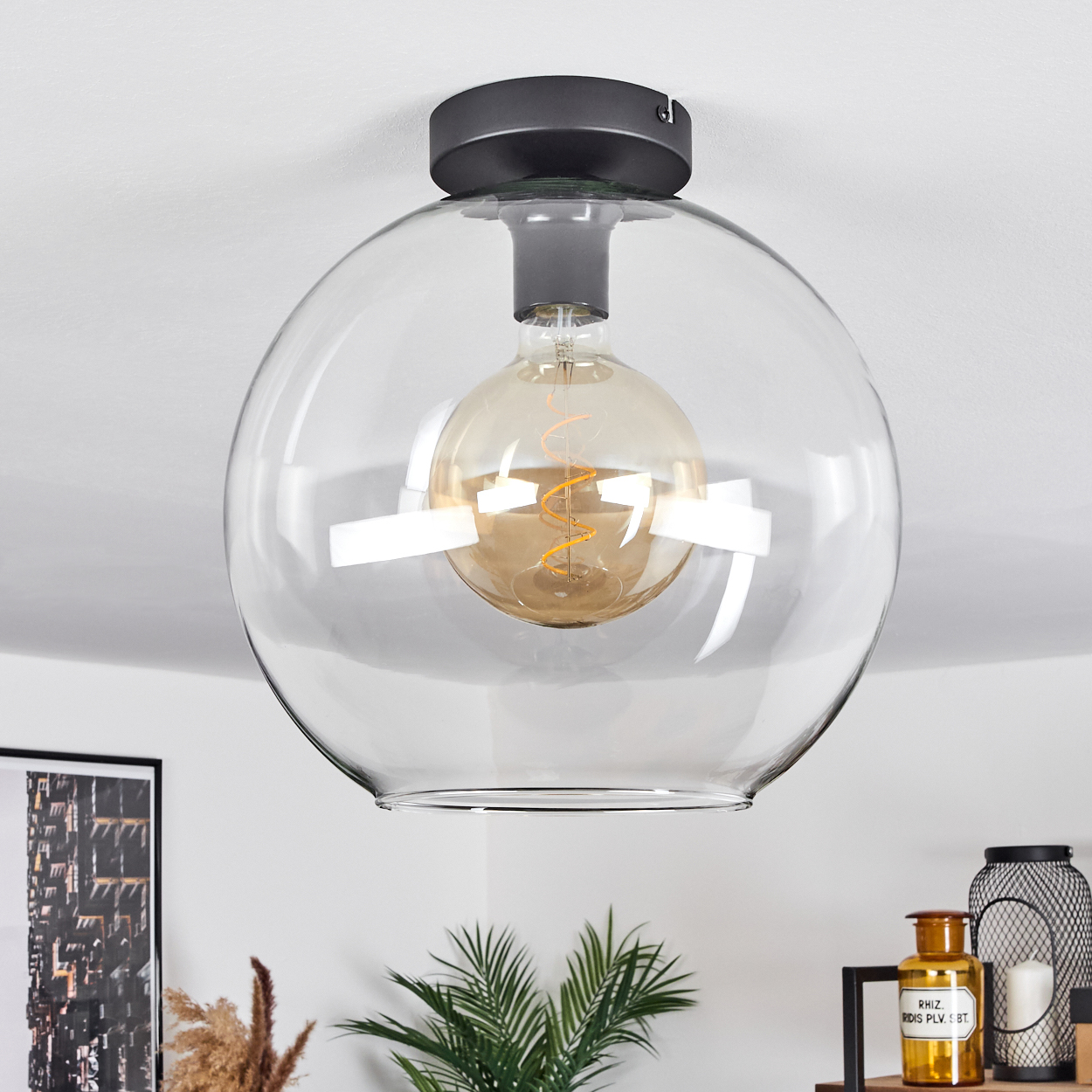 Eine klare, kugelförmige Deckenlampe aus Glas mit einer warmen Glühbirne. Die Lampe ist auf einem schwarzen Sockel montiert. Weitere Dekorationen sind unten sichtbar.