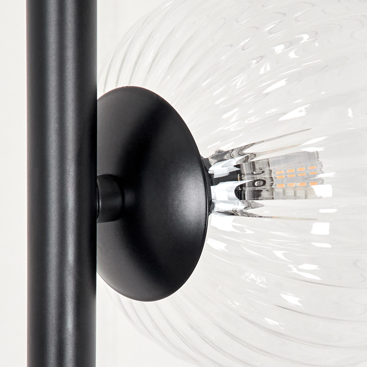 Nahaufnahme einer Lampe. Schwarze Metallsäule und kreisförmige Basis halten eine klare, gerippte Glaskugel.