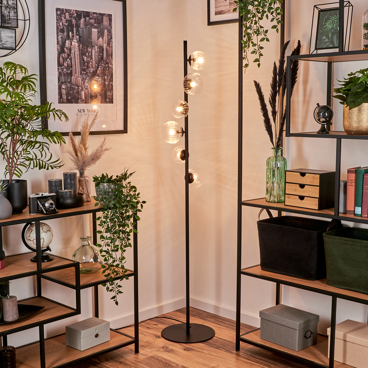 Eine Zimmerecke mit Stehlampe, Regalen mit Pflanzen, Büchern und Deko, und einem Foto von New York City.