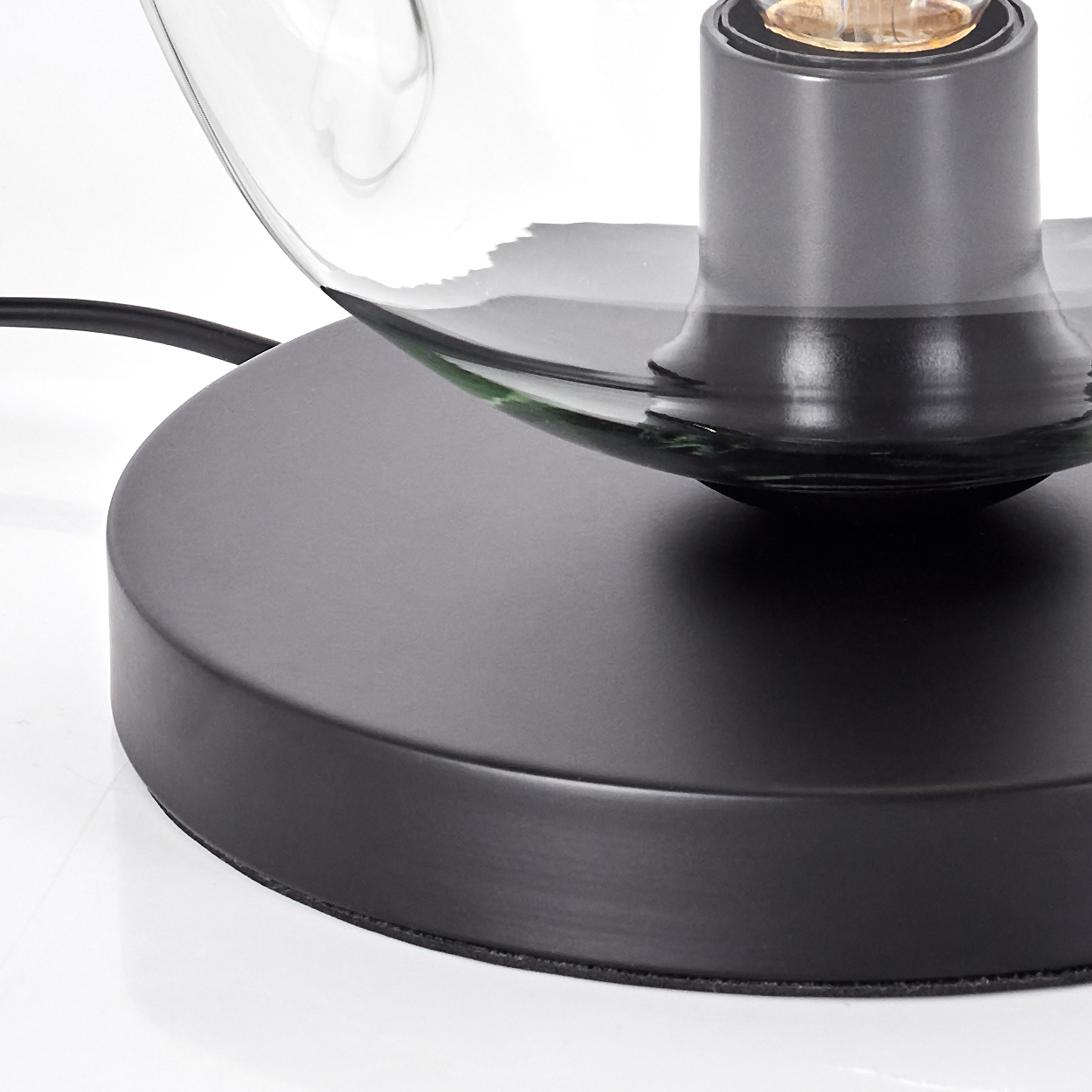Nahaufnahme einer schwarzen Tischlampe. Die Lampe hat einen runden Sockel, einen klaren Glasschirm und eine sichtbare Glühbirne.