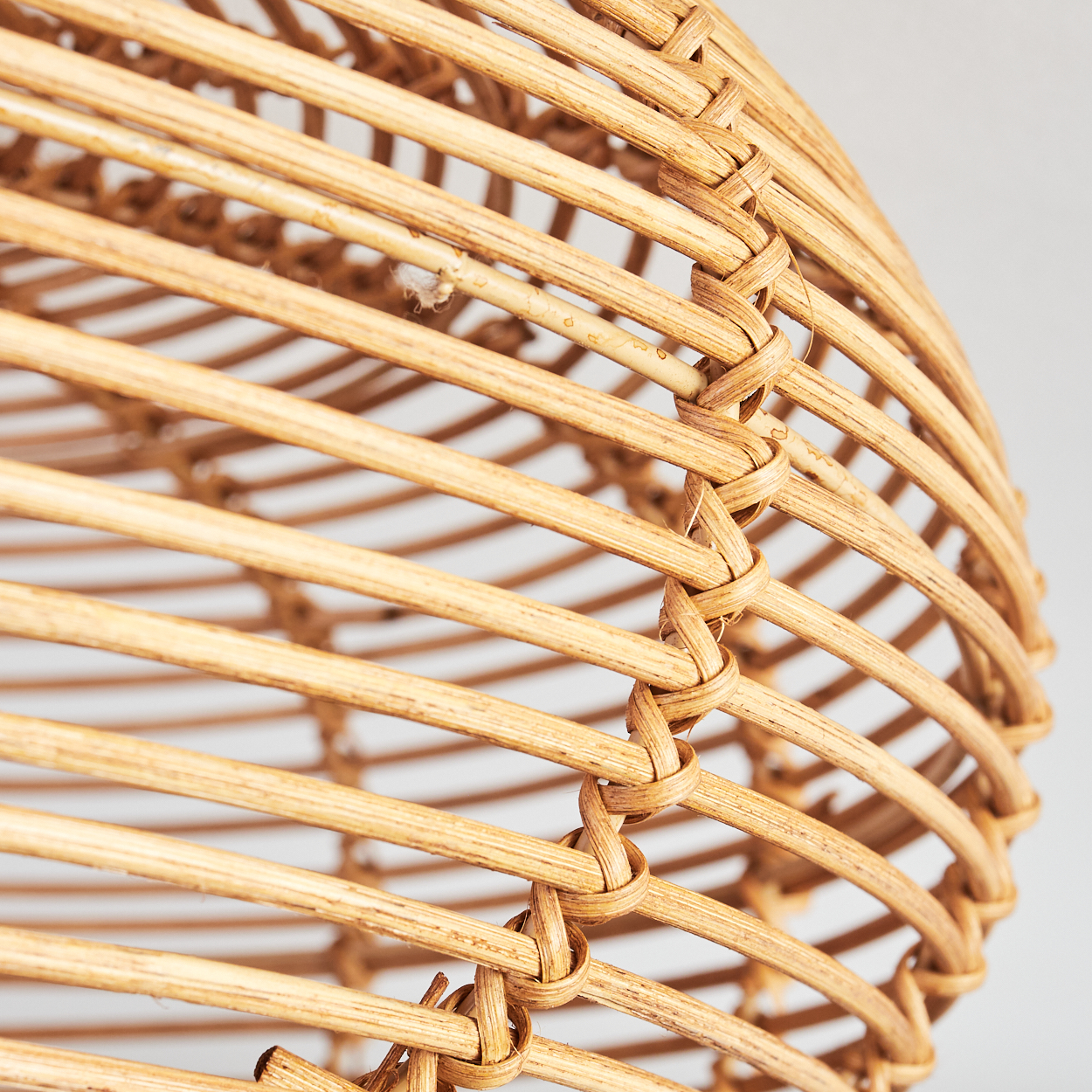 Nahaufnahme eines gewebten Lampenschirms aus Rattan. Das hellbraune Material ist aufwendig gewebt, mit sichtbaren Knoten und einer gebogenen Form.