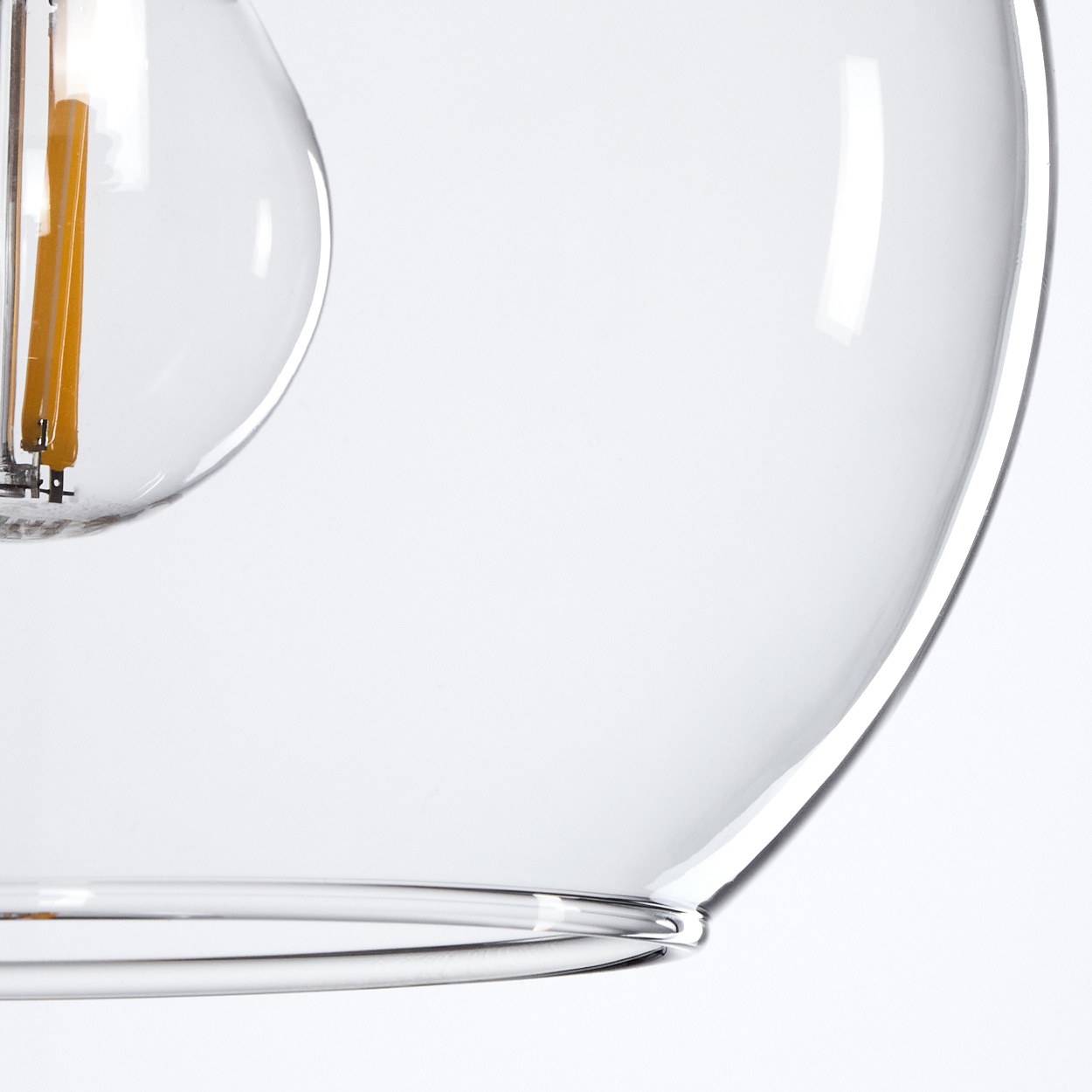Nahaufnahme einer Glasleuchte. Ein klarer, runder Glasschirm. Im Inneren eine Glühbirne mit warm getöntem Filament.