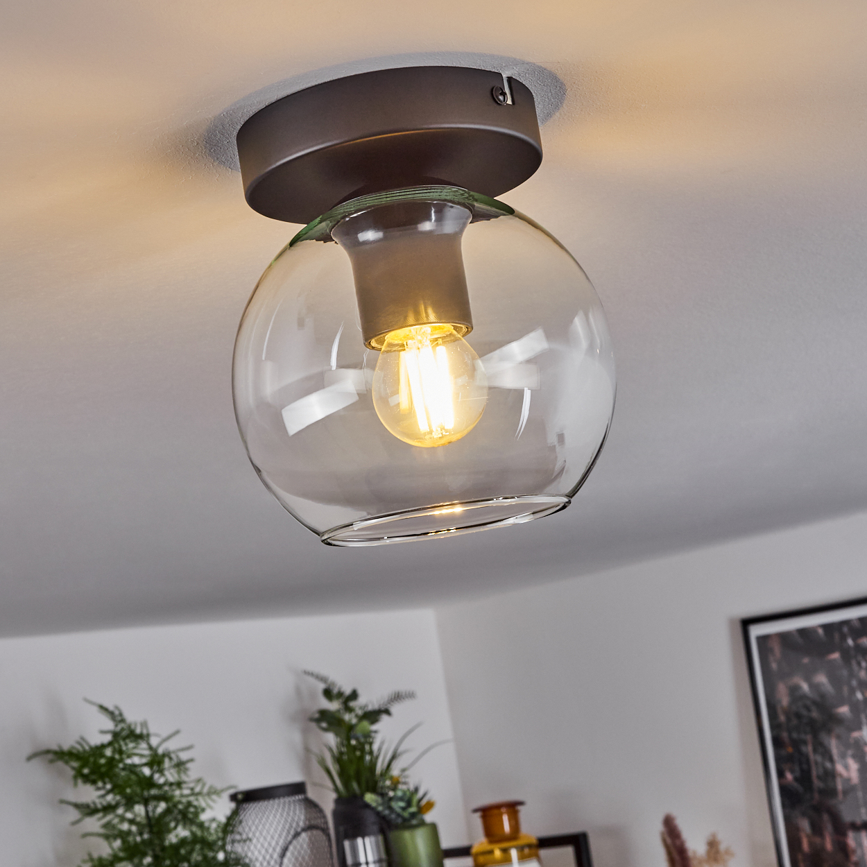 Eine moderne Deckenleuchte mit Glaskugelschirm und einer leuchtenden Glühbirne. Die Leuchte ist an einer weißen Decke befestigt.