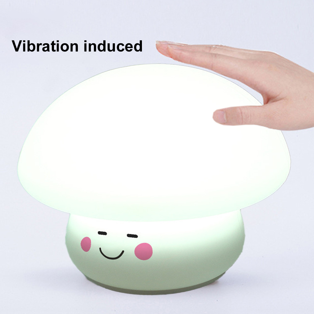 Eine pilzförmige Lampe wird von einer Hand berührt. Sie hat ein lächelndes Gesicht mit rosa Wangen. Der Text lautet 'Vibrationsinduziert'.