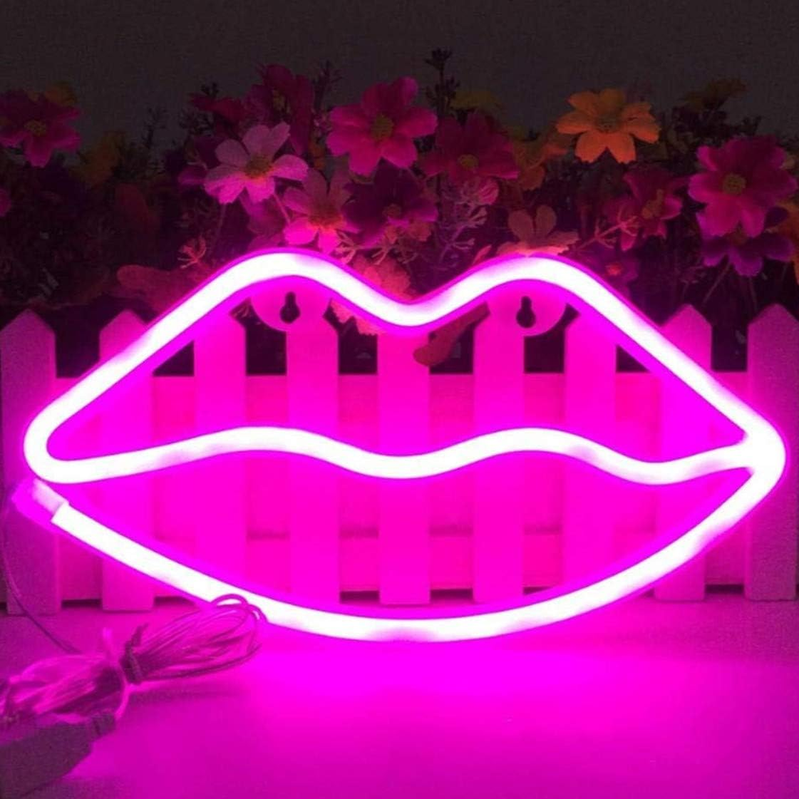 Ein neonrosa Lippenschild vor einem weißen Gartenzaun mit bunten Blumen im Hintergrund.