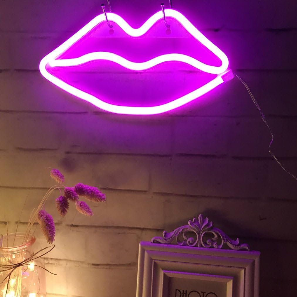 Ein neonrosa Lippenschild hängt an einer Ziegelmauer. Darunter befinden sich eine Vase mit Blumen und ein Bilderrahmen.