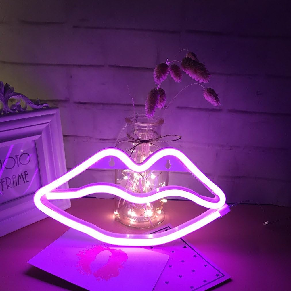 Ein neonfarbenes Lippenschild leuchtet rosa. Dahinter steht ein Glas mit Lichterketten und Trockenblumen auf einem Tisch.