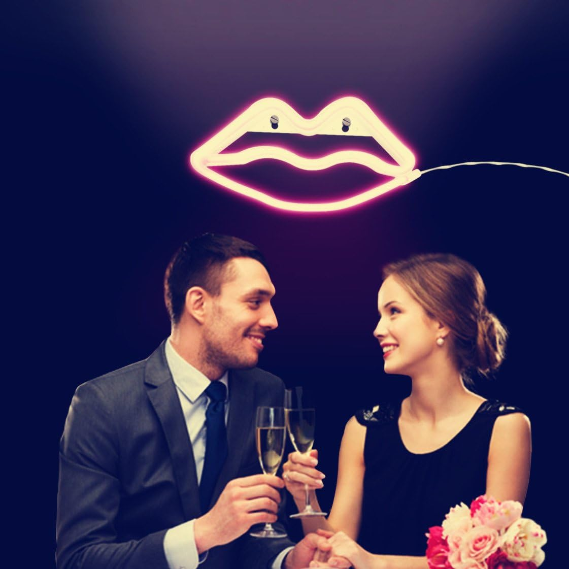 Ein Paar prostet mit Champagner unter einem Neon-Lippenschild an. Blumen auf dem Tisch. Der Mann trägt einen Anzug, die Frau ein schwarzes Kleid.