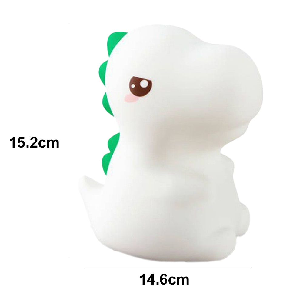 Eine weiße Dinosaurierlampe mit grünen Stacheln, braunen Augen und rosafarbenen Wangen. Sie ist 15,2 cm hoch und 14,6 cm breit.