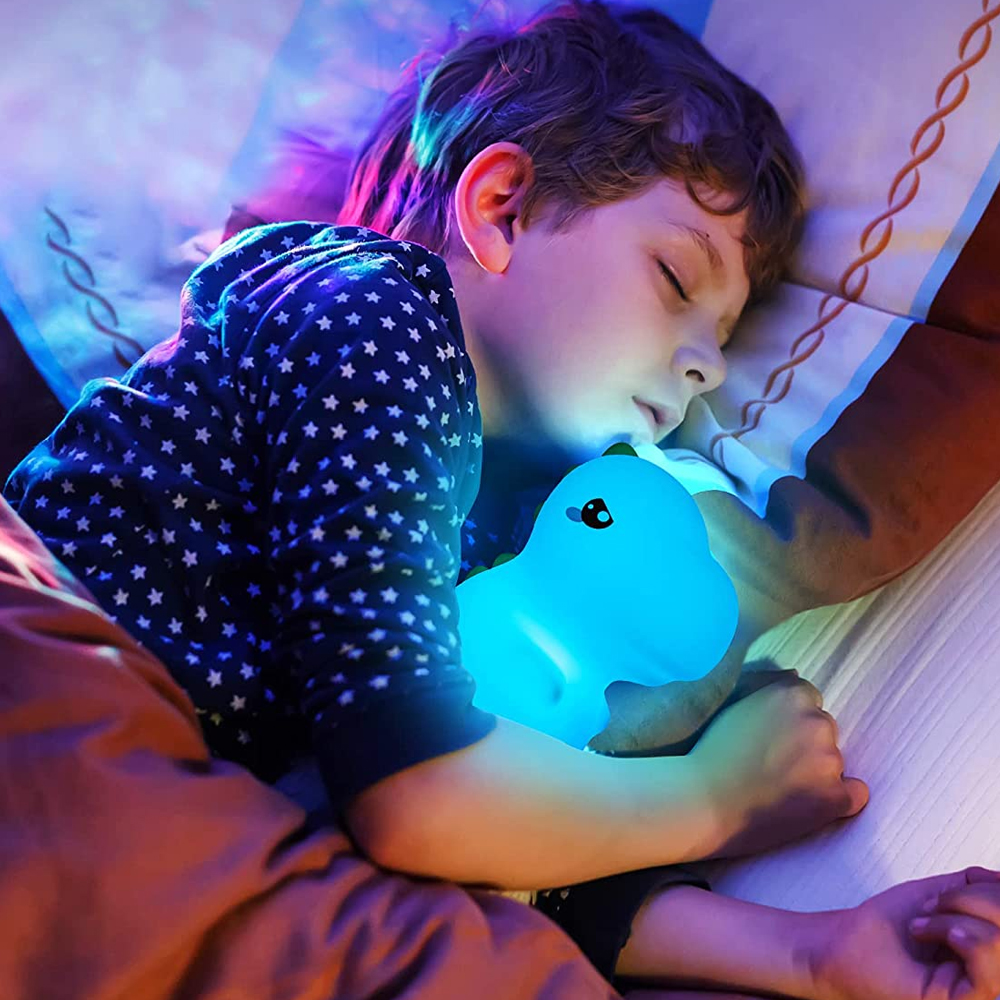 Ein Kind schläft und umarmt ein leuchtendes, blaues Pinguin-Nachtlicht in Sternenmuster-Pyjamas.