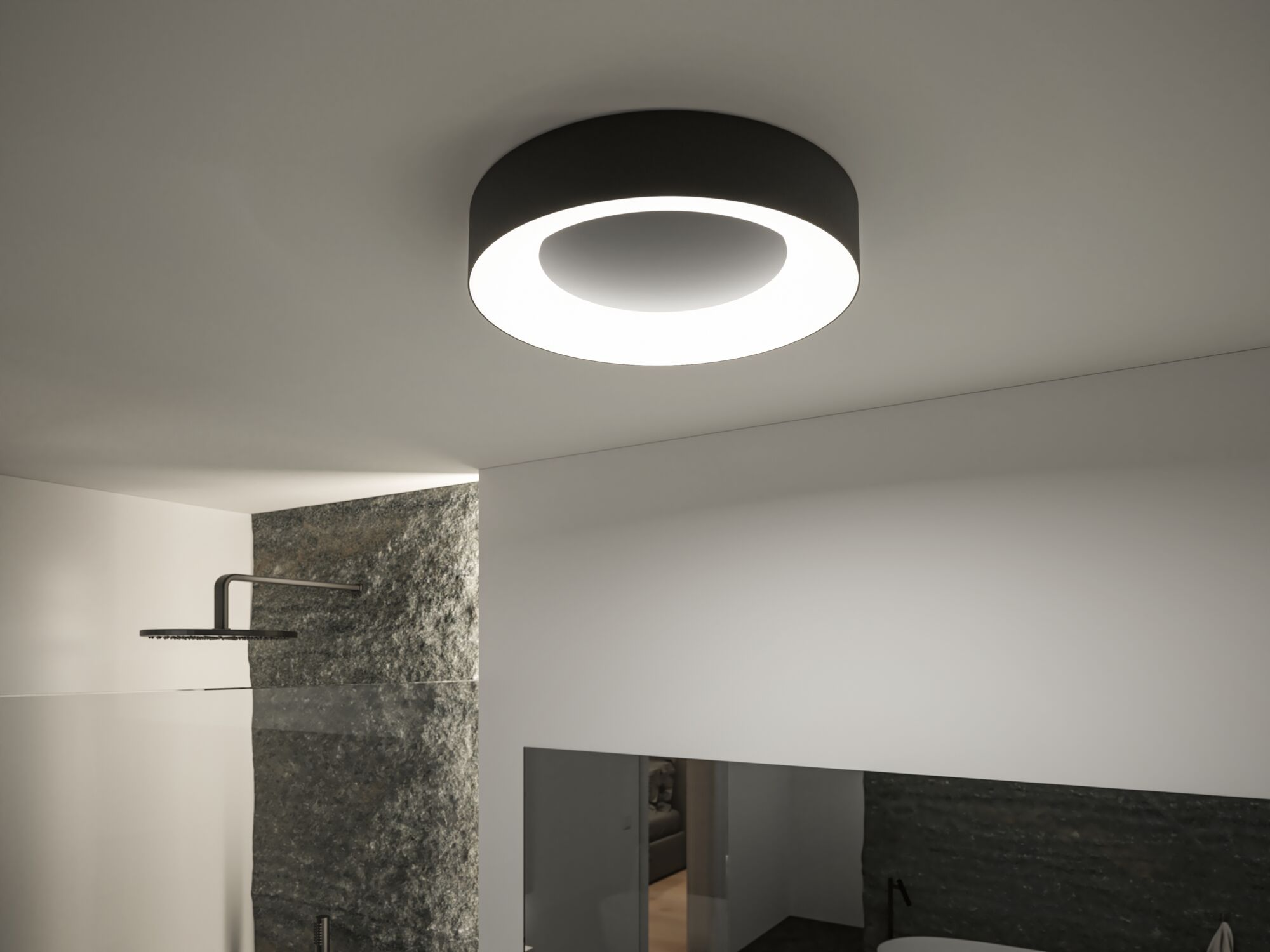 Nowoczesna łazienka z okrągłą lampą sufitową. Kamienna ściana z boku. Widoczna głowica prysznicowa. Białe ściany i sufit.