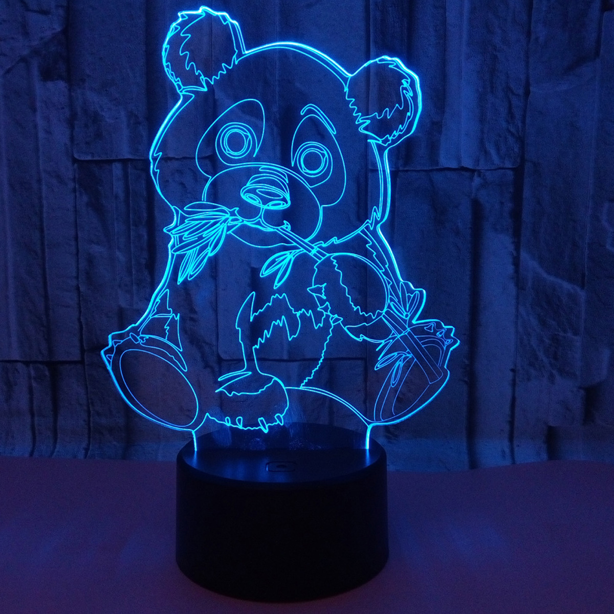 Eine blaue Neon-Pandalampe. Der Panda hält Bambus. Sie steht auf einem schwarzen Sockel vor einem Ziegelmauer-Hintergrund.